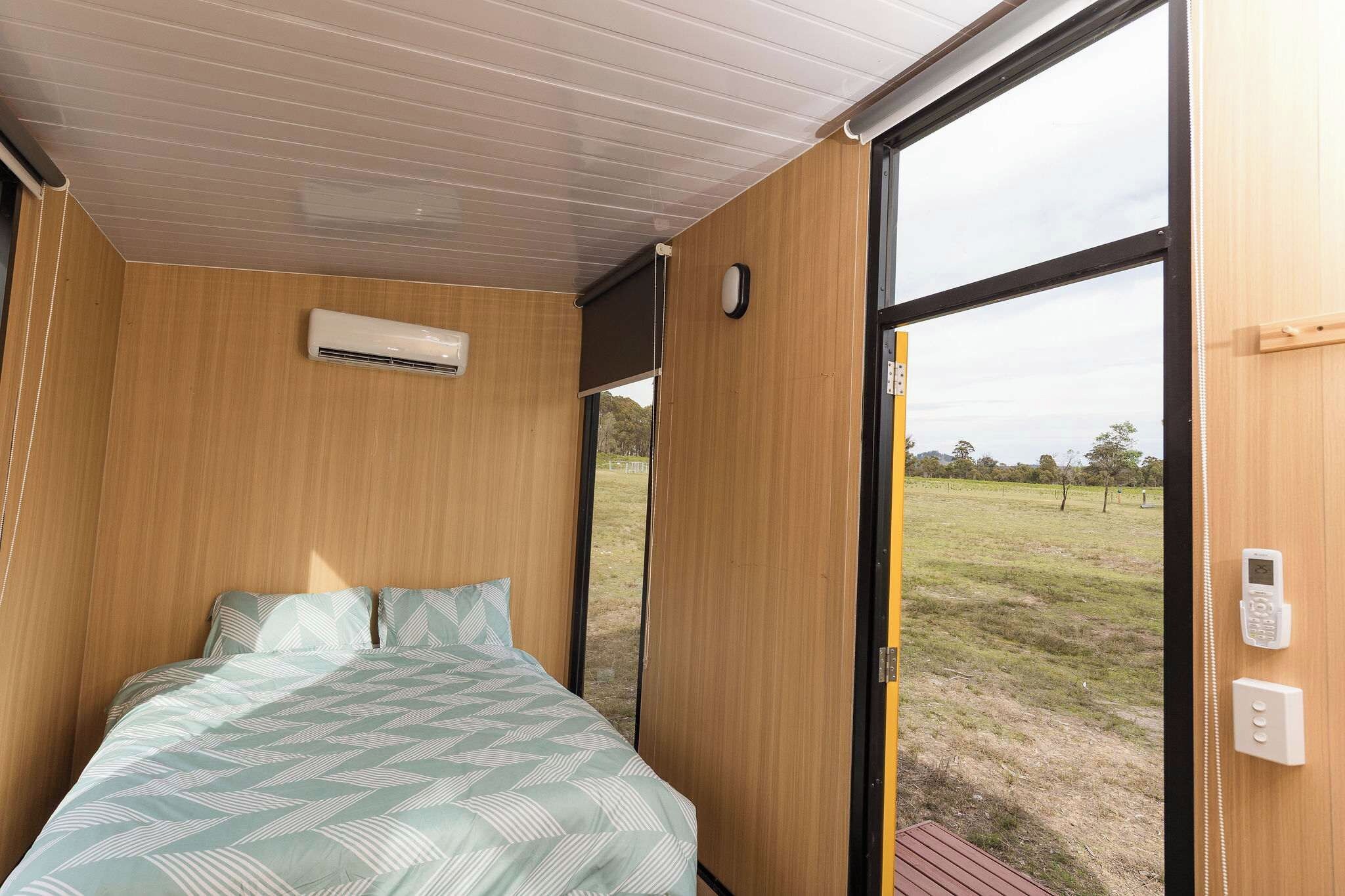 A bedroom with a bed, an air conditioning unit, a window, and a door leading outside.