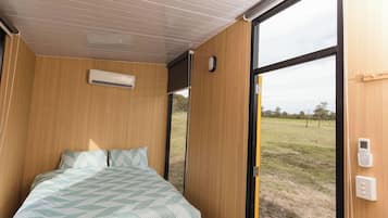 Une chambre à coucher comprenant un lit, un appareil de climatisation, une fenêtre et une porte donnant sur l’extérieur.