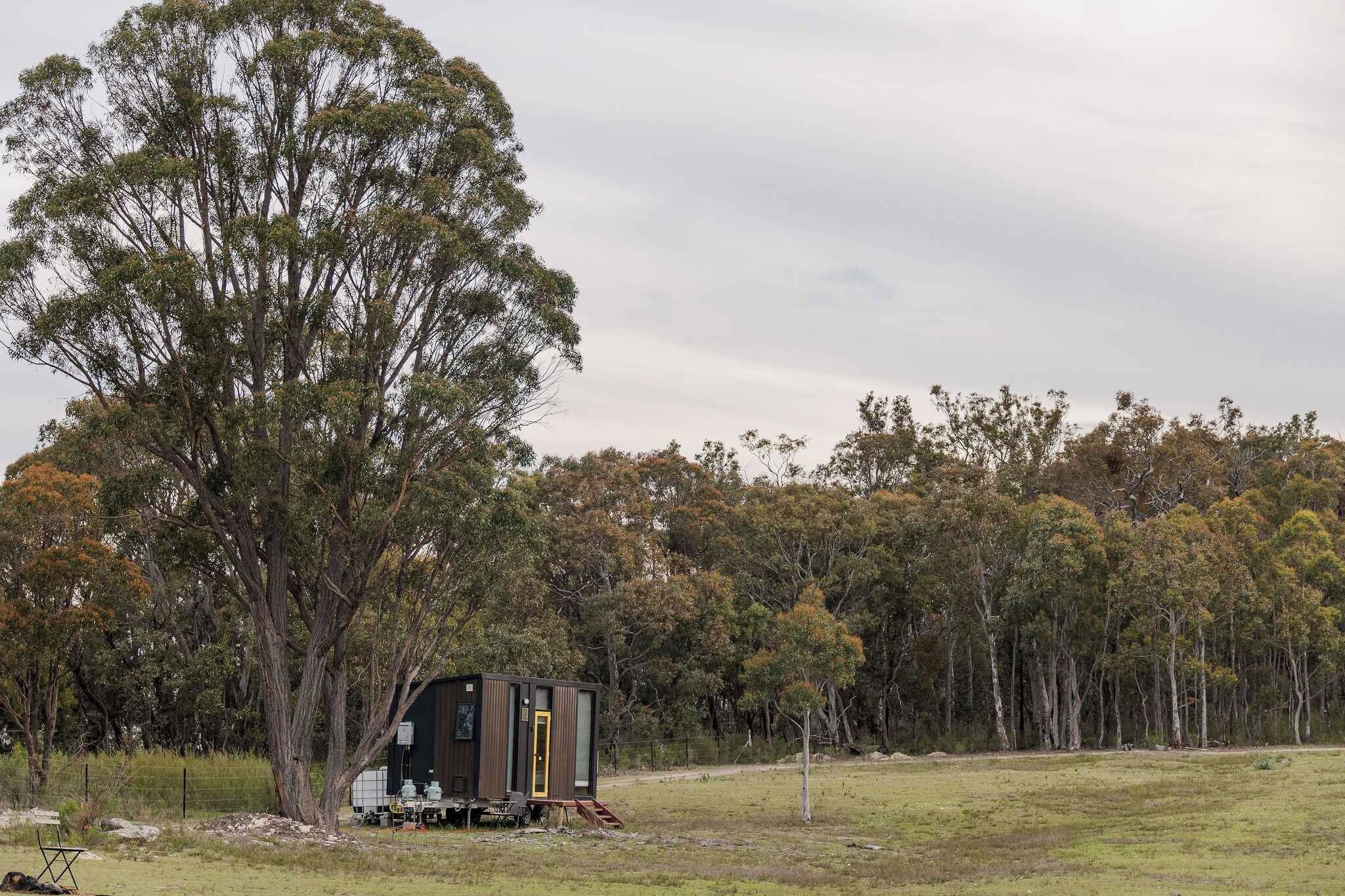 Une maison mobile de plain-pied, dotée d’un petit porche, située dans un champ verdoyant, avec une forêt dense en arrière-plan.