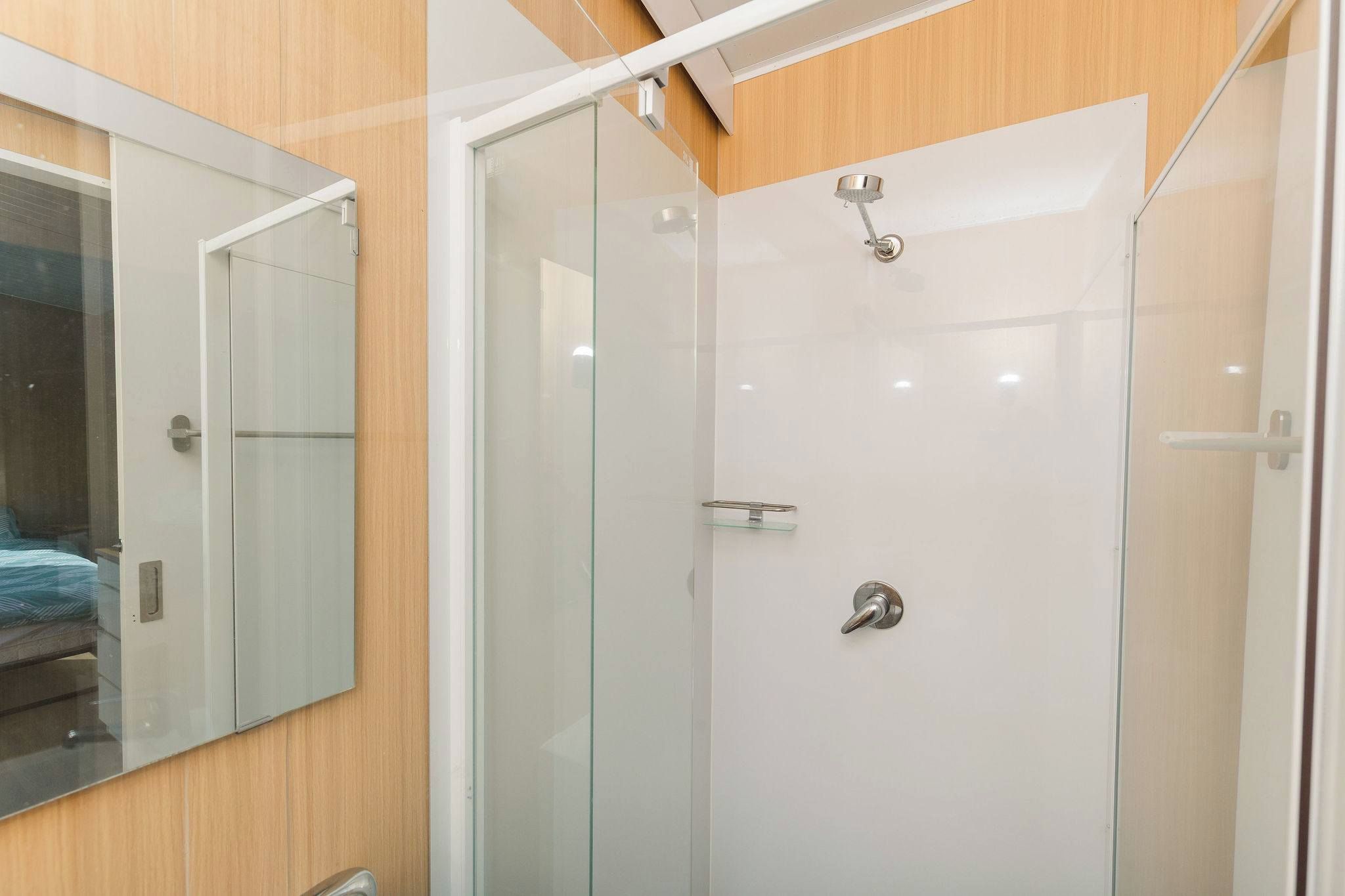 Une salle de bain moderne avec une douche à paroi de verre, un panneau mural en bois et un miroir.