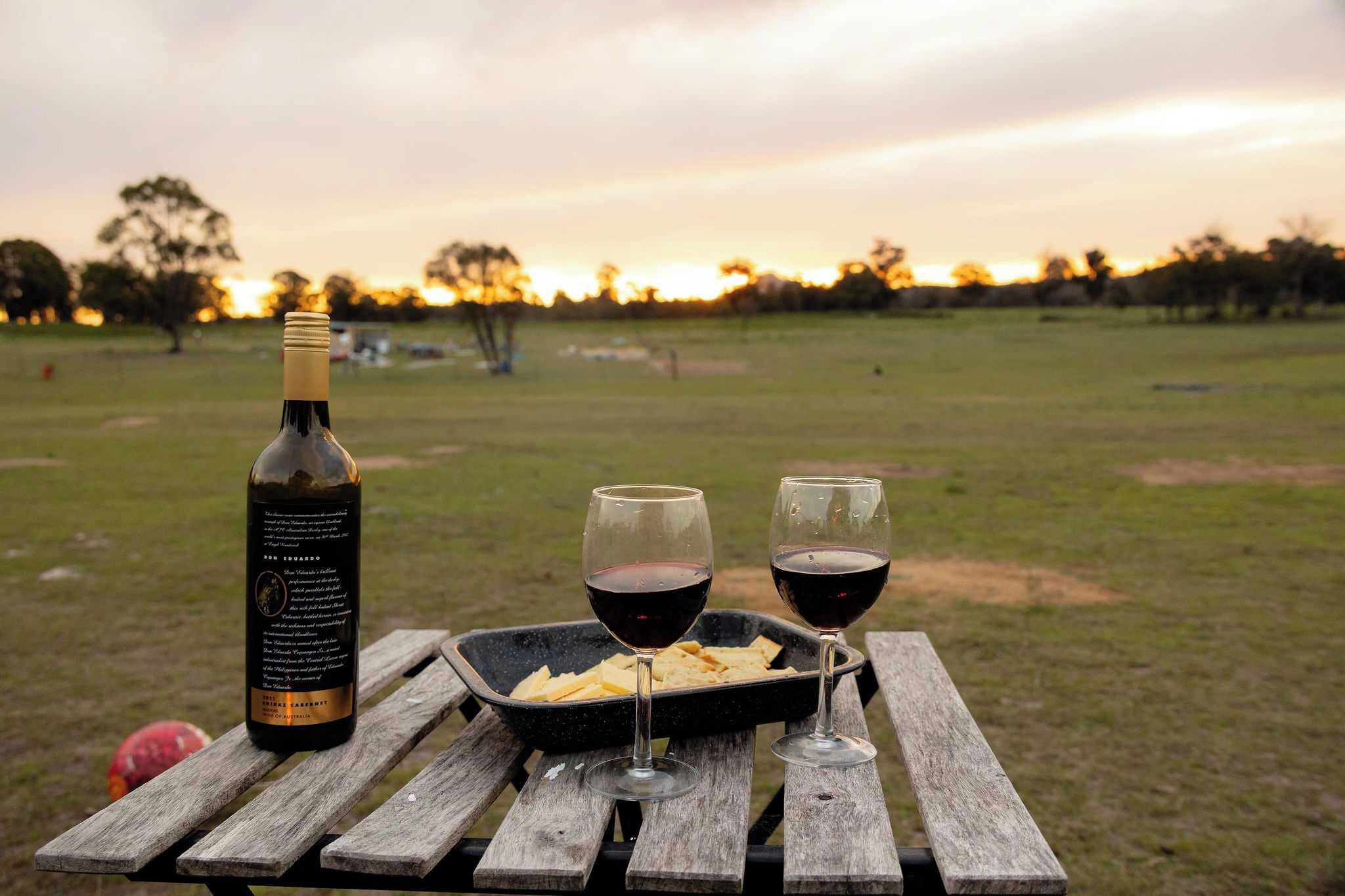 Une bouteille de vin, deux verres et une assiette de pain sur une table en bois, dans un cadre extérieur.