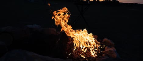 A campfire with logs and a bottle of wine, surrounded by rocks.