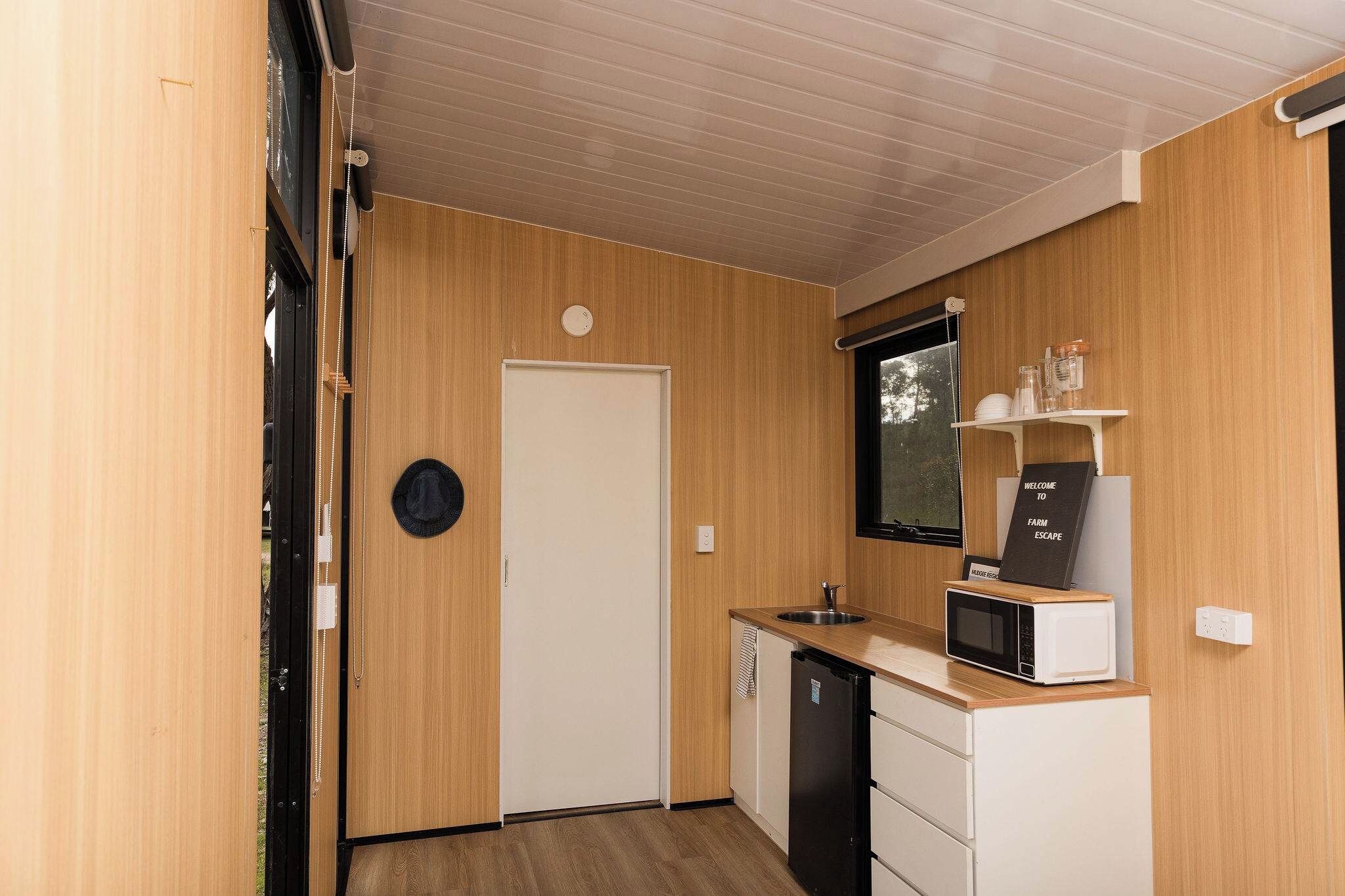 A compact kitchen with wooden walls, a white door, a microwave, and a sink.