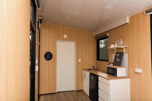 Eine kleine Küche mit Holzwänden, einer weißen Tür, einer Mikrowelle und einem Spülbecken.