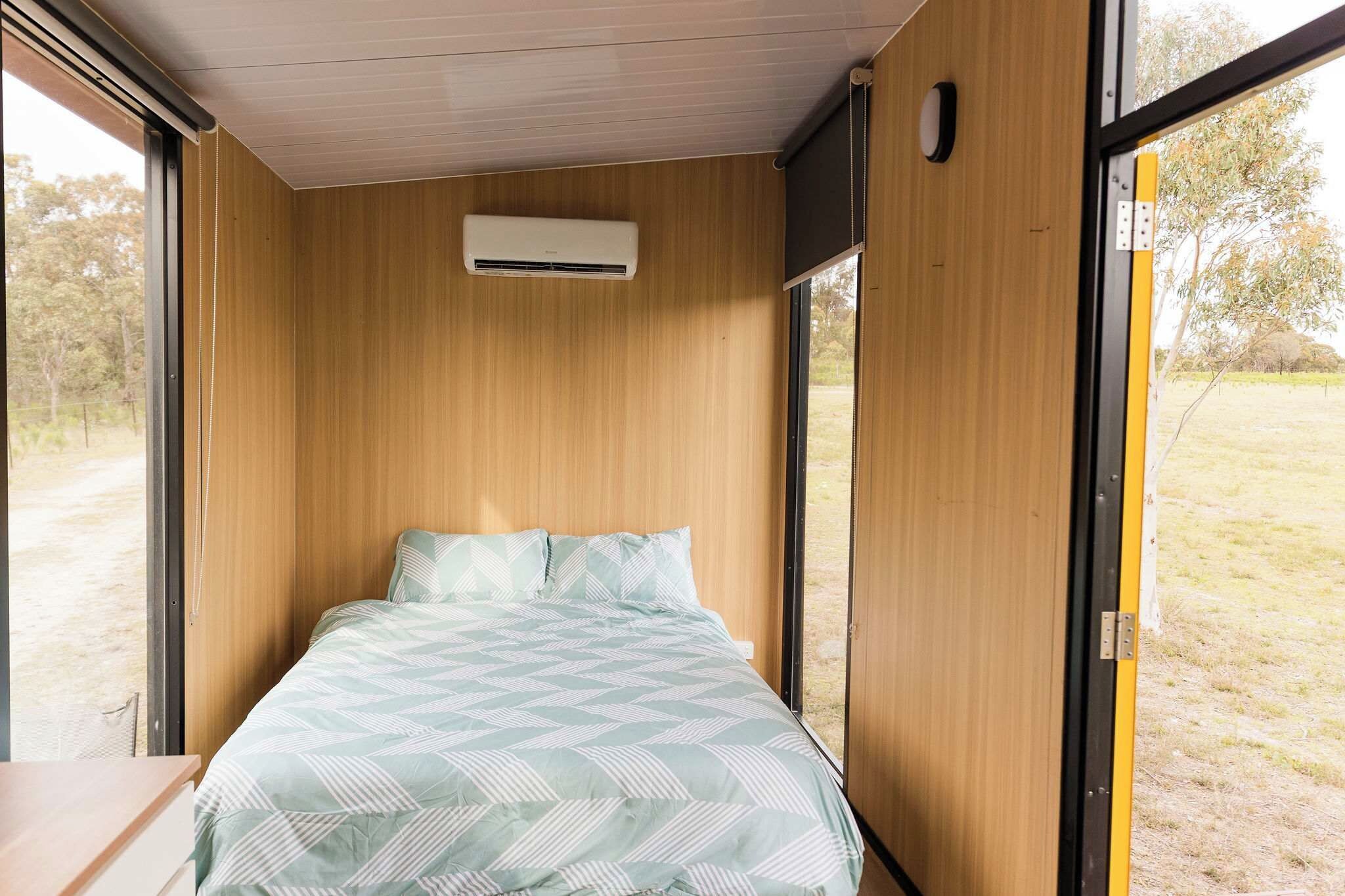 A single bed with a patterned bedspread in a room with wooden walls and a window.