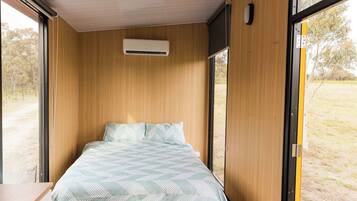 A single bed with a patterned bedspread in a room with wooden walls and a window.