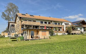 Un edificio de varios pisos con balcones, una zona de estar cubierta al aire libre y un césped.
