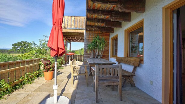 Eine Terrassenanlage im Freien mit Holztischen und -stühlen, einem roten Sonnenschirm und Topfpflanzen.