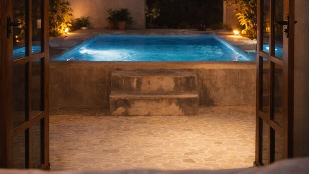 An open doorway leading to a swimming pool area at night with ambient lighting. - AJAW Cabana | Jungle, privacy and relaxation near Cancun (Leona Vicario)
