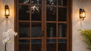 A wooden door with glass panels, flanked by two wall-mounted lights, a potted orchid, and a thatched roof. - AJAW Cabana | Jungle, privacy and relaxation near Cancun (Leona Vicario)
