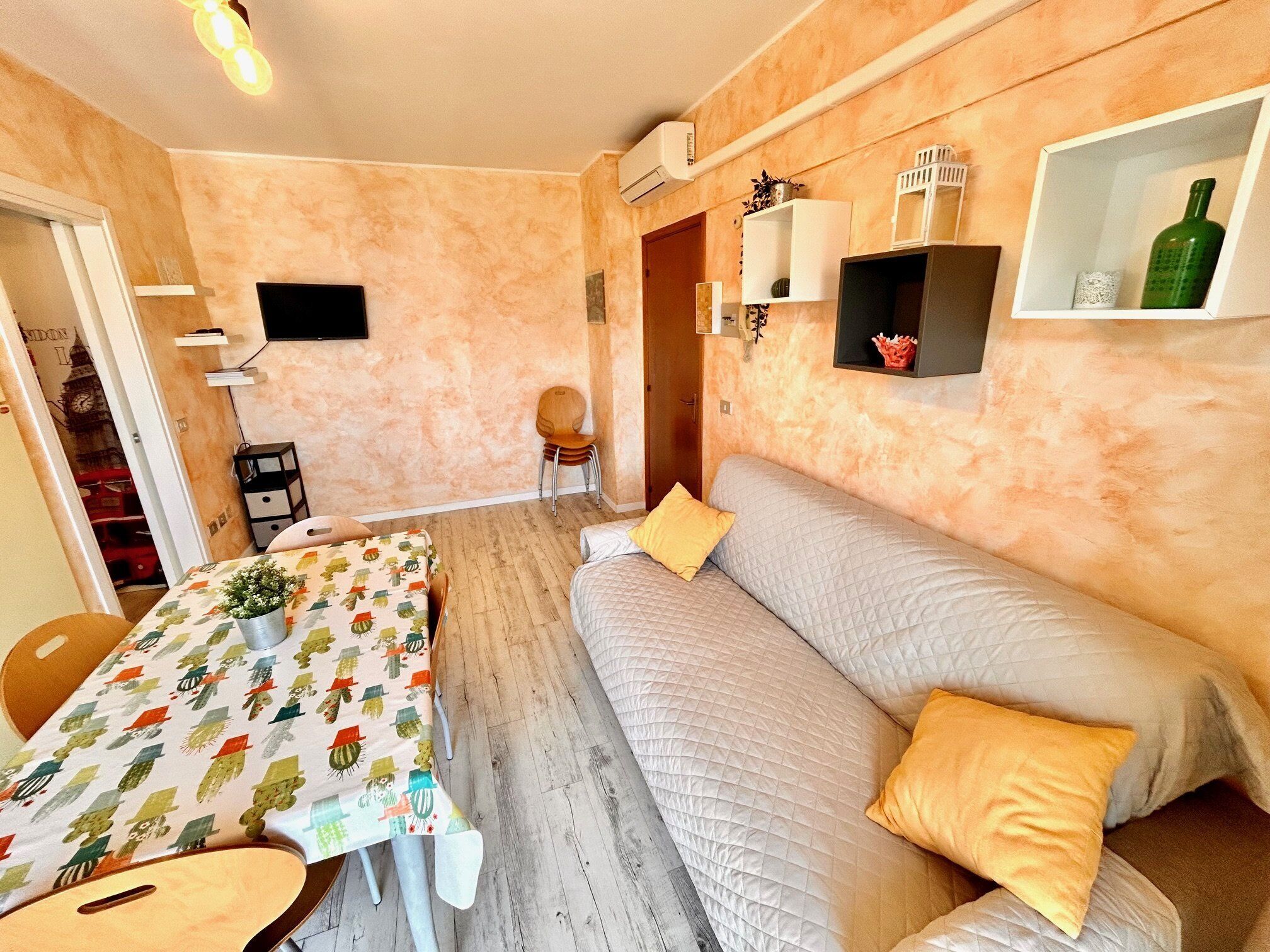 A cozy room with a dining table, a sofa, a TV, and a wall-mounted shelf with decorative items.