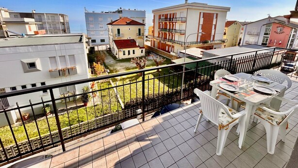 A balcony with a table and chairs, a view of buildings, and a fenced yard. - BILO PESARO MARCELLI - Two-room apartment with a/c just a stone's throw from the sea and the center (Marcelli)