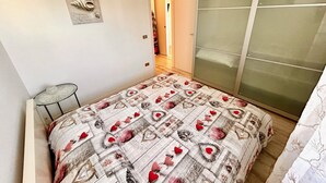 A bedroom with a bed, a small table, a wardrobe, and a door leading to another room. - BILO PESARO MARCELLI - Two-room apartment with a/c just a stone's throw from the sea and the center (Marcelli)