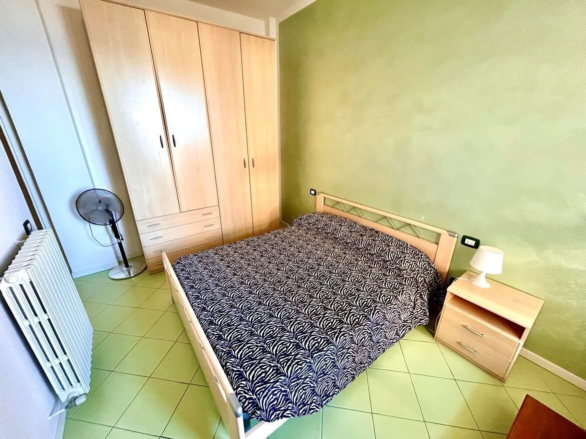 A bedroom with a bed, a wardrobe, a radiator, and a bedside table with a lamp.