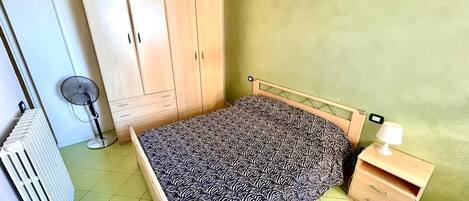 A bedroom with a bed, a wardrobe, a radiator, and a bedside table with a lamp.