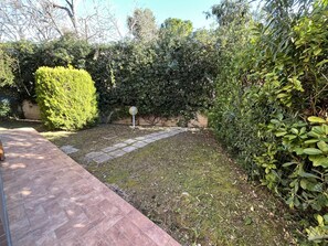 Ein Garten mit gepflastertem Weg, dichtem Grün und einer kugelförmigen Leuchte.