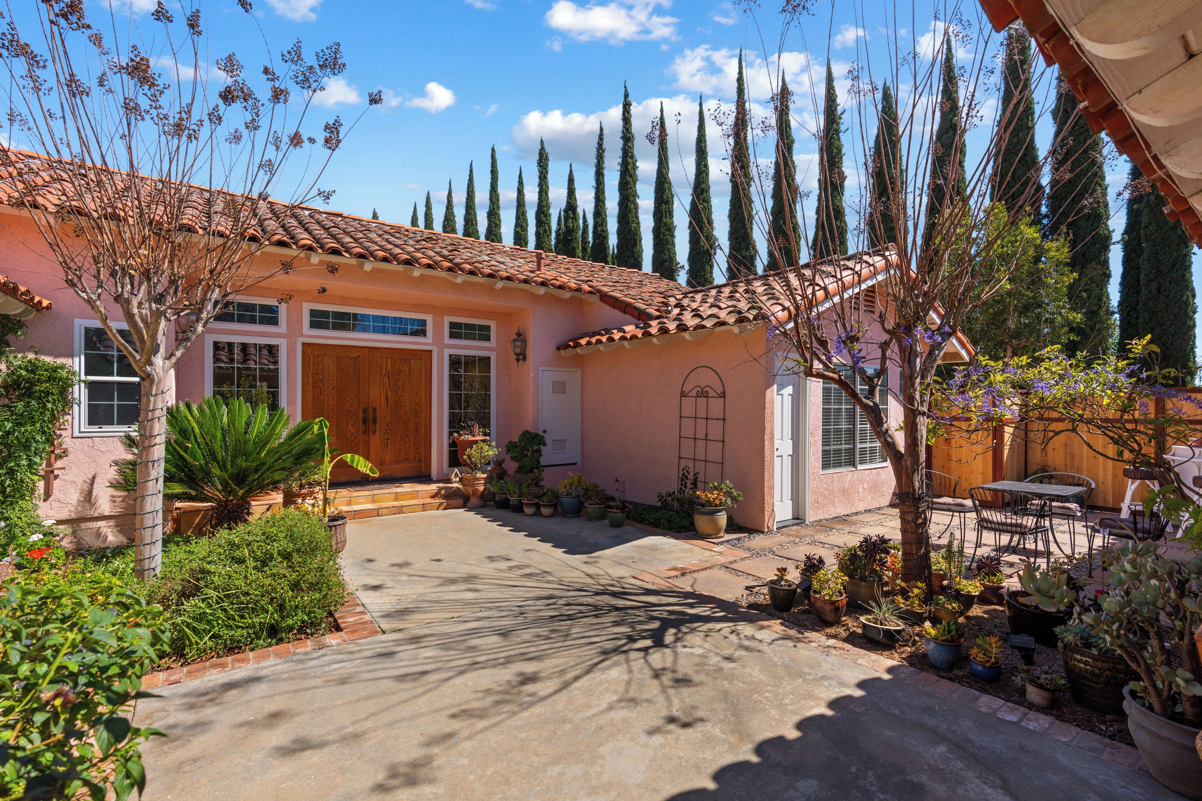Una casa con techo de tejas, puerta principal y un patio con plantas en macetas y una mesa.