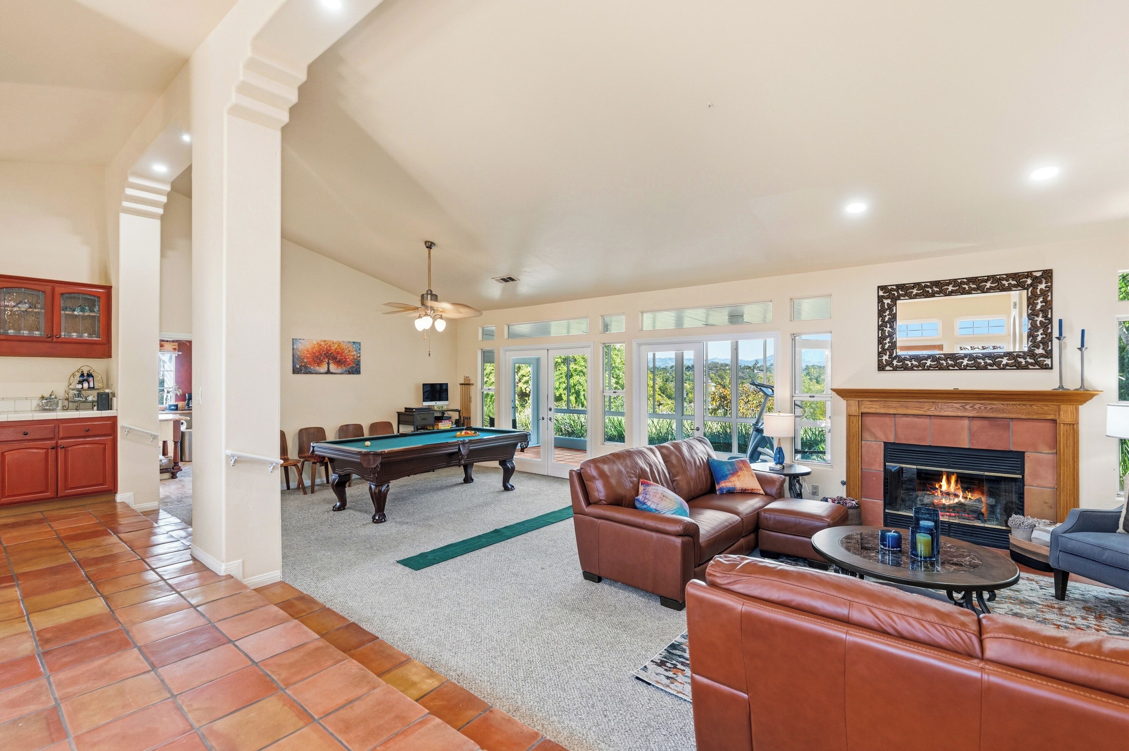 A spacious living room with a pool table, leather sofas, a fireplace, and large windows.