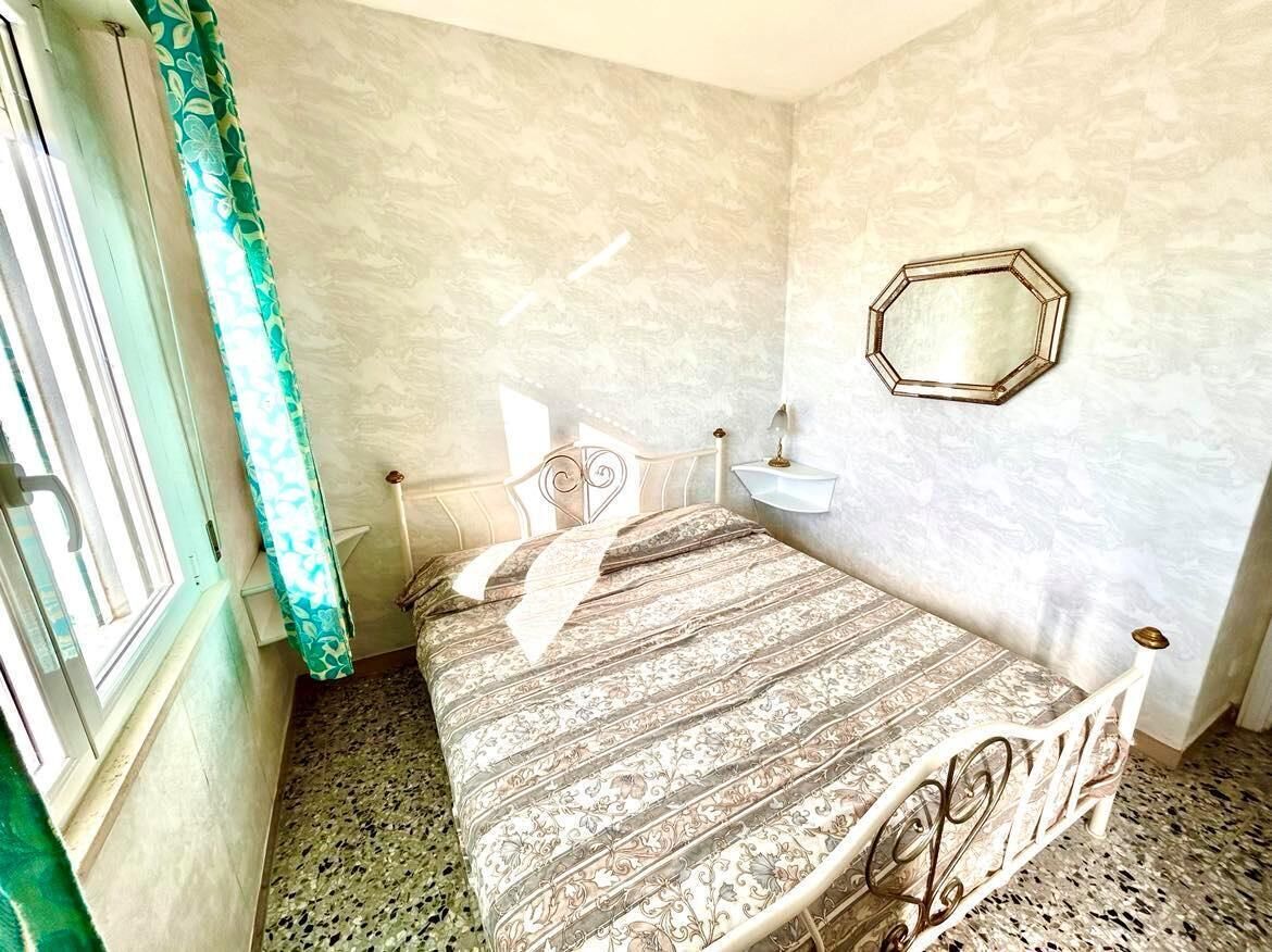 Une chambre à coucher avec un lit, une table de chevet, un miroir et une fenêtre avec des rideaux.