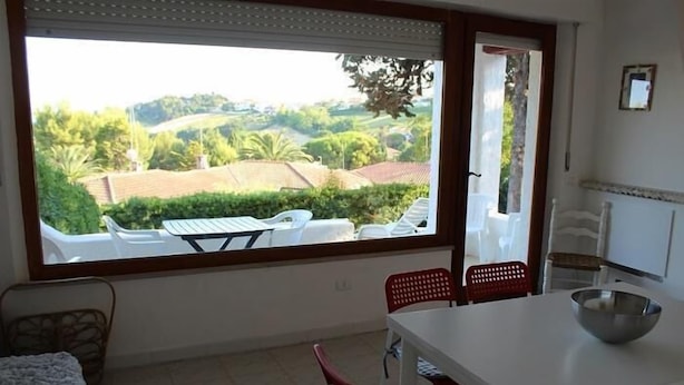 Ein Zimmer mit Esstisch, Stühlen, einem Fenster mit Blick auf Grünflächen und Gebäude sowie einer Heizung.