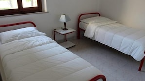 Ein Zimmer mit zwei Einzelbetten, einem kleinen Nachttisch mit Lampe und einem Fenster.