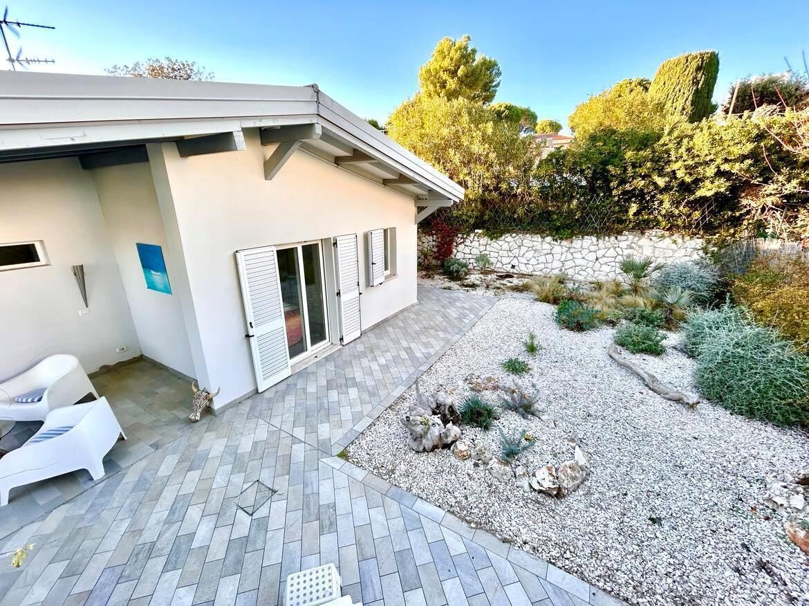 A modern house with a patio area, a stone wall, and a garden with various plants.
