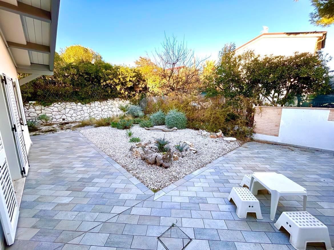 Un espace patio agrémenté d’un chemin en pierre, de meubles d’extérieur blancs et d’un jardin où poussent différentes plantes, le tout bordé d’un mur en pierre.