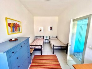 Une chambre avec deux lits, une commode, une petite table et une porte donnant sur un balcon.