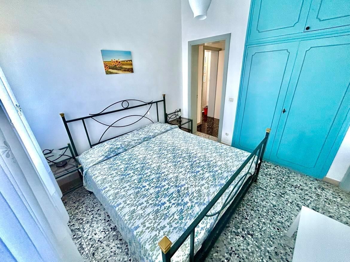 Un dormitorio con una cama, una puerta azul, una mesita pequeña y un cuadro en la pared.