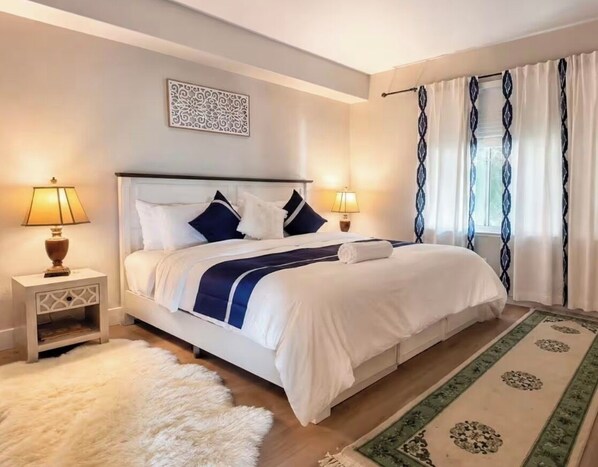 A bedroom with a bed, two bedside tables, a rug, and a window with curtains.