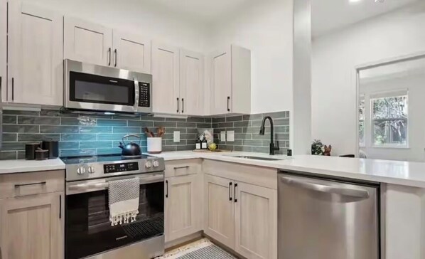 A modern kitchen with stainless steel appliances, light wood cabinets, and a tiled backsplash.