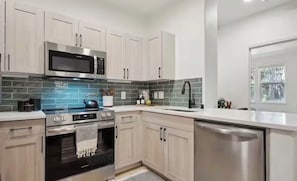 Une cuisine moderne dotée d’appareils électroménagers en acier inoxydable, de meubles de couleur bois clair et d’un revêtement mural en carreaux.