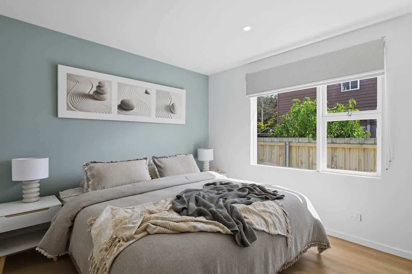 Une chambre à coucher avec un lit, des lampes de chevet, une fenêtre donnant sur un paysage verdoyant et des œuvres d’art murales.