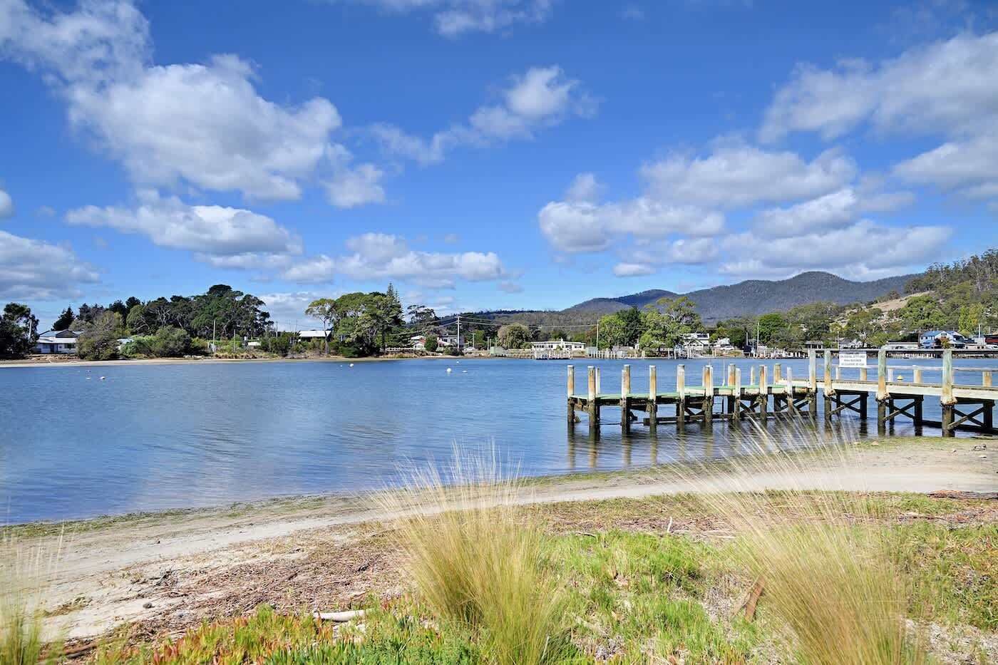 A calm lake with a wooden pier extending into the water, surrounded by greenery and distant hills.