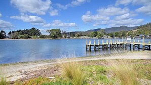 Un lago tranquilo con un muelle de madera que se adentra en el agua, rodeado de vegetación y colinas a lo lejos.