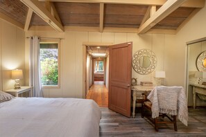 A bedroom with a bed, a desk, a chair, a mirror, and a view of a garden through a window. - a luxurious and elegantly appointed 4-bed, 4-bath home situated on 1.83 acres (Little River)