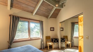 Ein Schlafzimmer mit einem Bett, zwei Stühlen, einem Spiegel und einem Fenster mit Vorhängen.