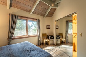 Ein Schlafzimmer mit einem Bett, zwei Stühlen, einem Spiegel und einem Fenster mit Vorhängen.
