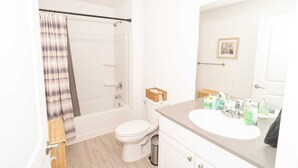 Et badeværelse med bruser, toilet, vask og spejl.