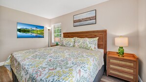 Un dormitorio con una cama, una mesita de noche con una lámpara y dos cuadros colgados en la pared.