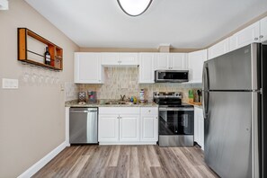 Une cuisine moderne avec des meubles blancs, des appareils en acier inoxydable et un plancher en bois.