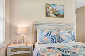 Une chambre à coucher avec un lit, une table de chevet avec une lampe, un tableau au mur et une fenêtre avec des stores.