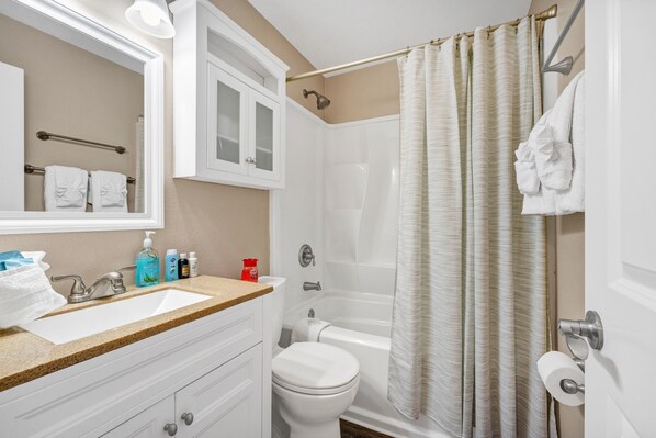 A bathroom with a sink, toilet, shower, and a mirror.