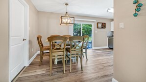 Un comedor con una mesa y sillas de madera, una lámpara colgante y vistas al exterior.