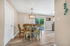 Un espace repas avec une table et des chaises en bois, un luminaire suspendu et une vue sur l’extérieur.