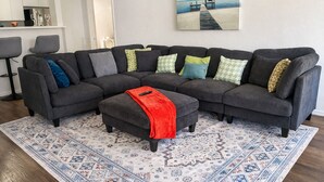 A sectional sofa with a red throw blanket, a patterned rug, and a painting of a pier on the wall. - Cozy 2B2B in Downtown PHX • Near Airport • Perfect Work or Getaway• (Phoenix)