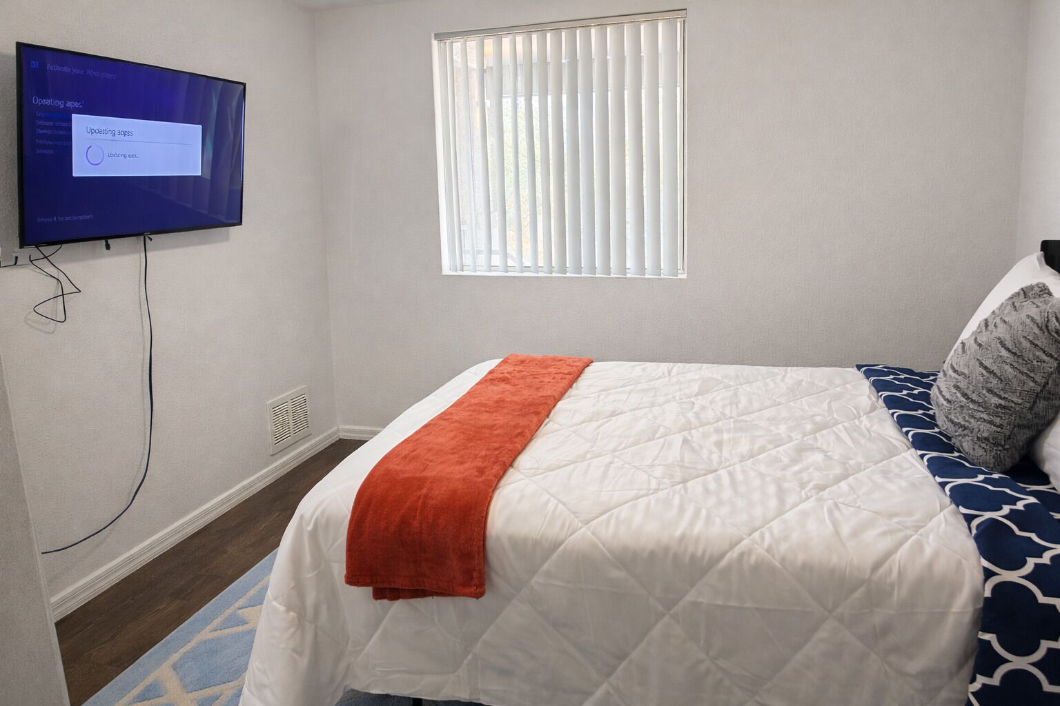 Ein Schlafzimmer mit einem Bett, einem an der Wand montierten Fernseher, einem Fenster mit Jalousien und einer Heizung.