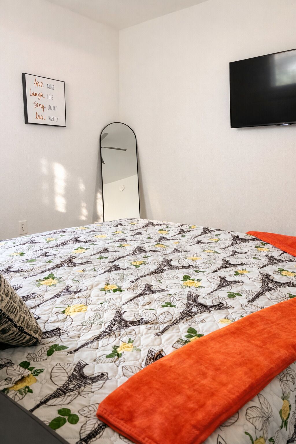 A bedroom with a bed, a mirror, a wall-mounted TV, and a motivational quote.