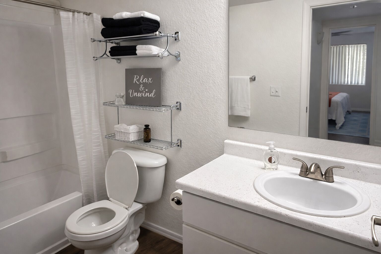Un bany amb vàter, un lavabo, un mirall i prestatges amb tovalloles i productes de higiene personal.