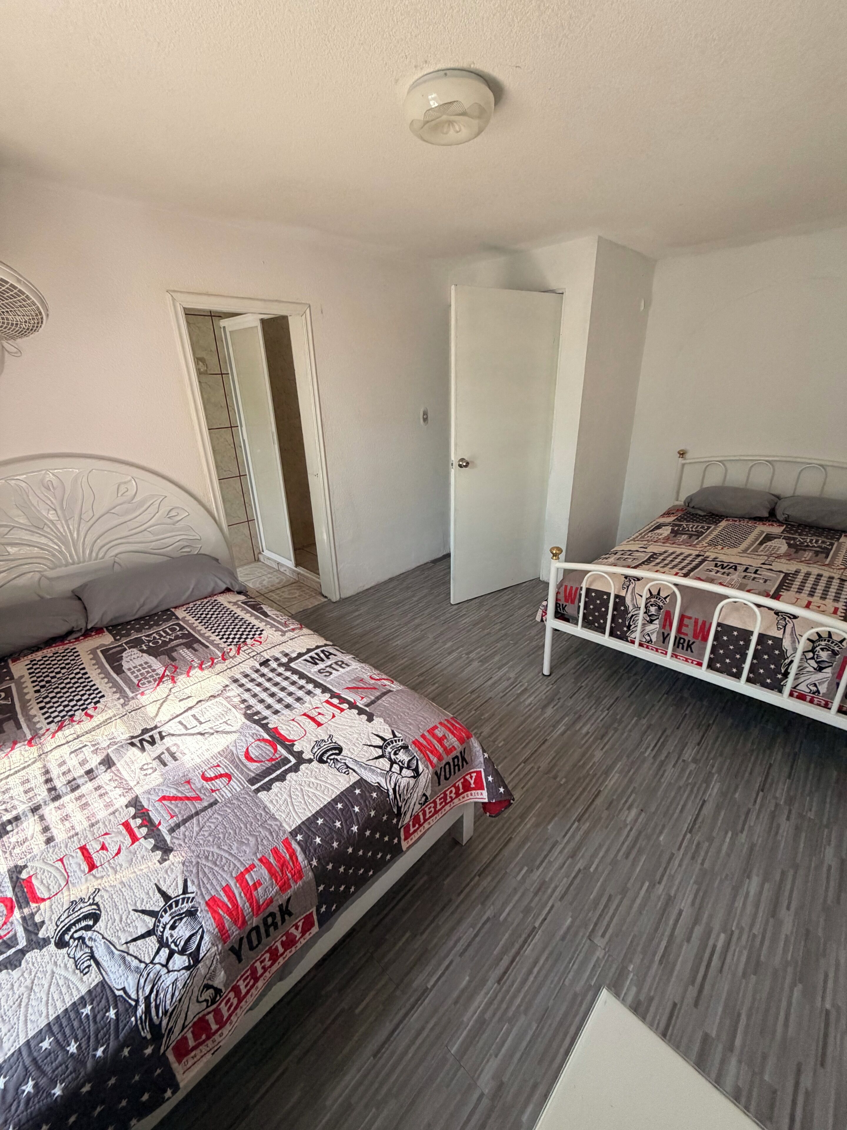 Et soveværelse med to senge, en dør og en loftlampe.